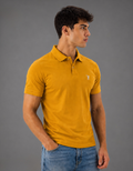 Man wearing a mustard yellow polo shirt with a logo on a gray background