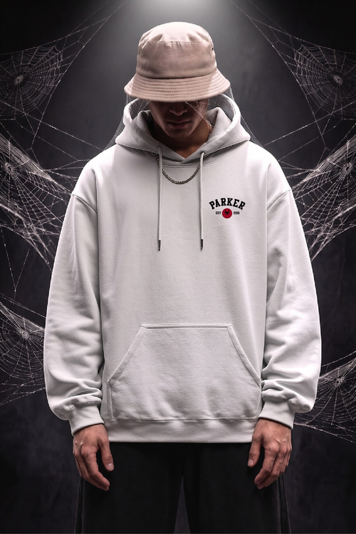 A person wearing a light gray pullover hoodie with a drawstring hood and kangaroo pocket, a beige bucket hat, and dark pants, standing against a dark background with spiderweb graphics. The hoodie has a small chest graphic reading 'PARKER' with a red circle logo.