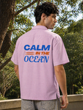 Person wearing a pink shirt with 'Calm in the Ocean' text on the back, standing outdoors.