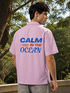 Person wearing a pink shirt with 'Calm in the Ocean' text on the back, standing outdoors.