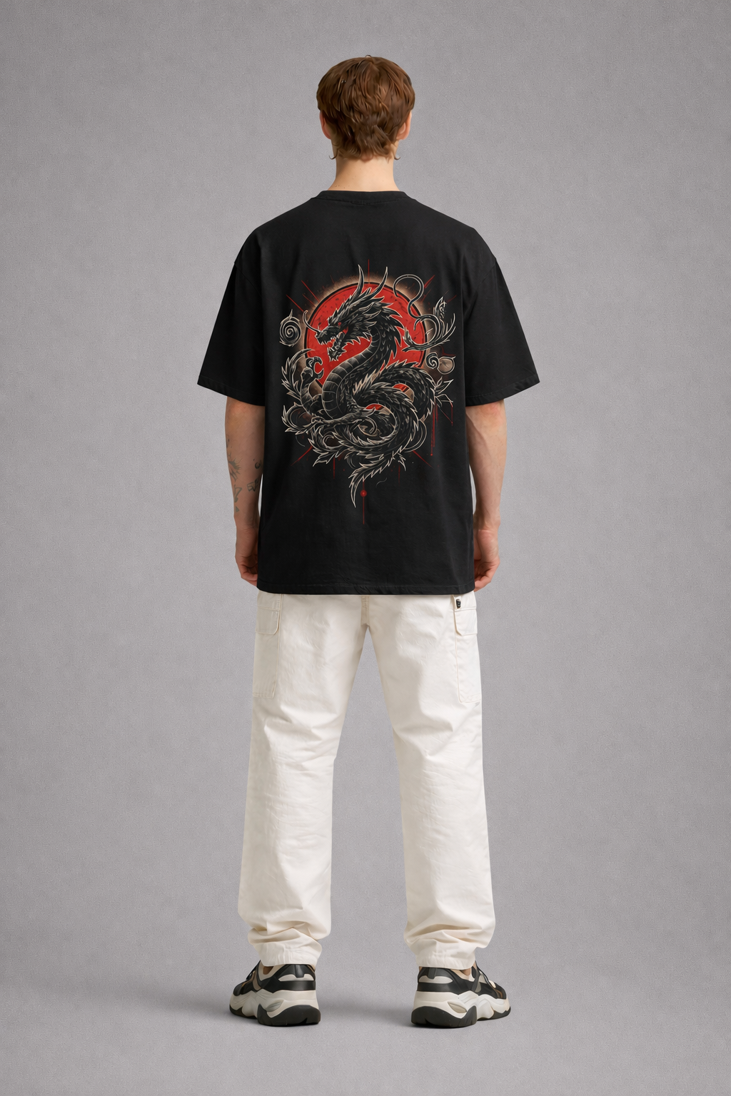 Person wearing a black t-shirt with a red and gray dragon design on the back, standing against a gray background.