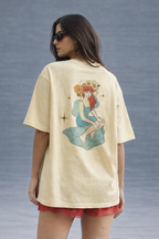 Woman wearing a beige t-shirt with a colorful graphic on the back against a gray background