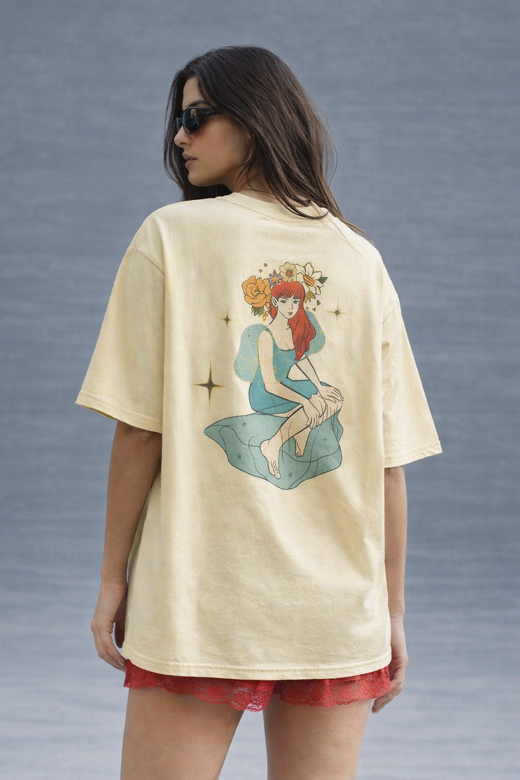 Woman wearing a beige t-shirt with a colorful graphic on the back against a gray background