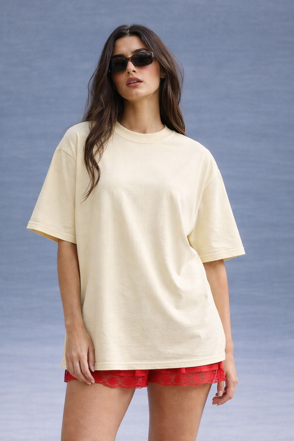 Woman wearing a beige oversized t-shirt and red shorts against a gray background