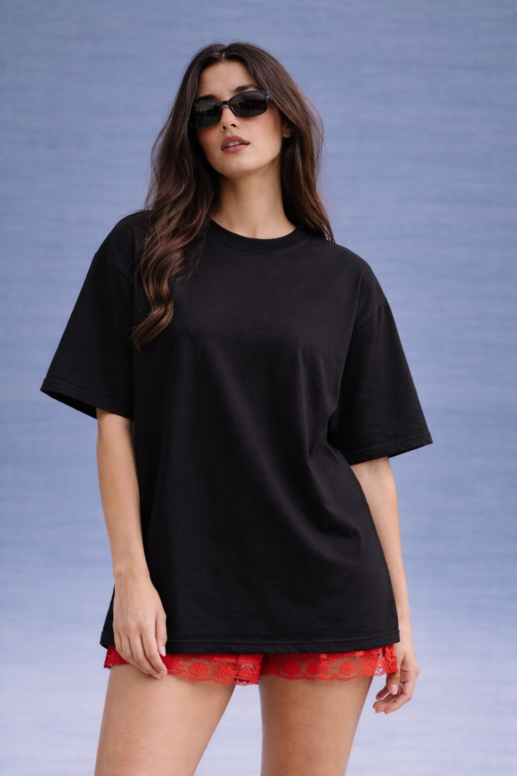 Woman wearing a black oversized t-shirt and red plaid shorts against a blue background