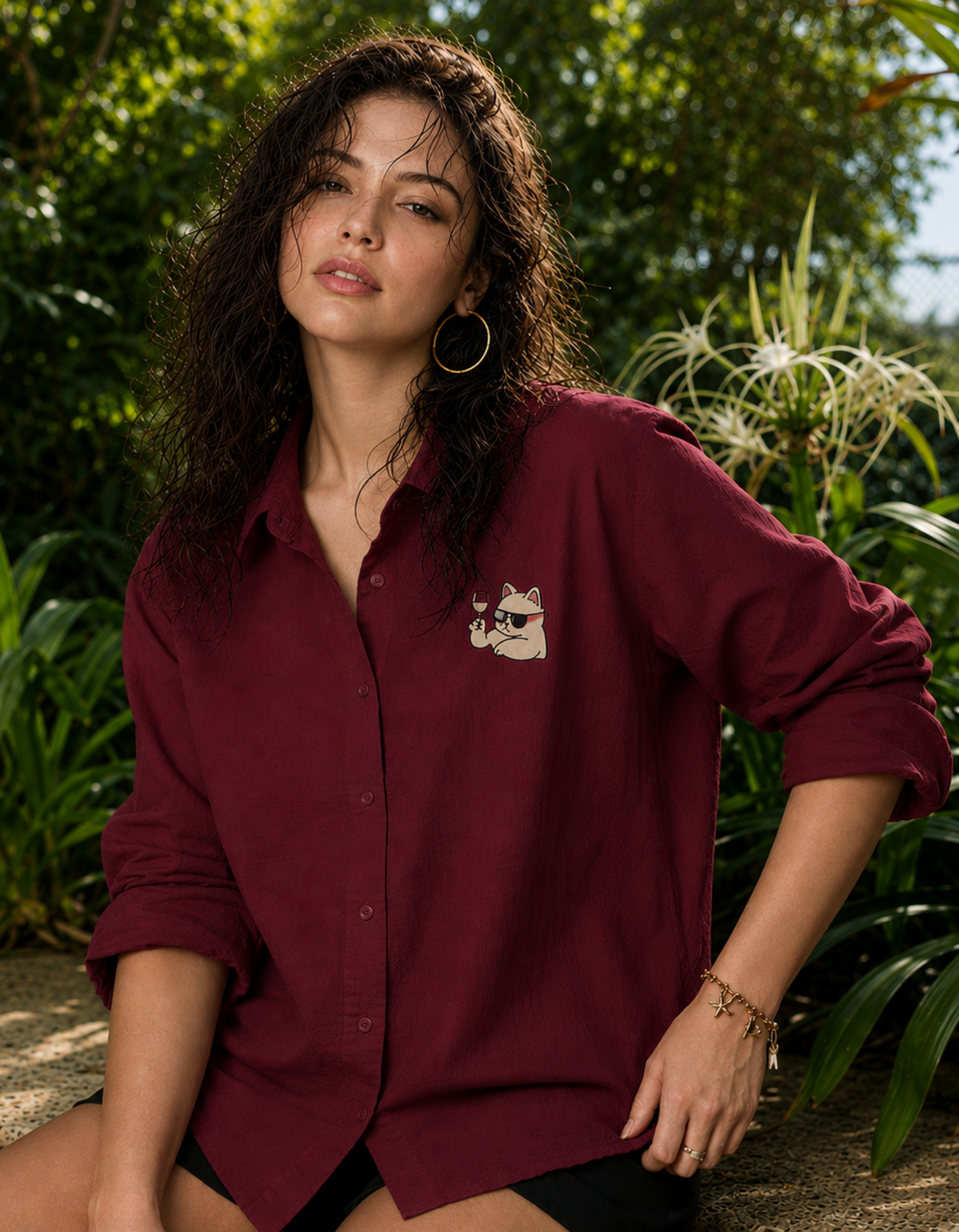Woman wearing a burgundy shirt with a cat emblem in a natural setting