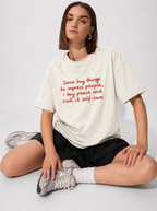 Person wearing a white t-shirt with red text sitting on the floor.