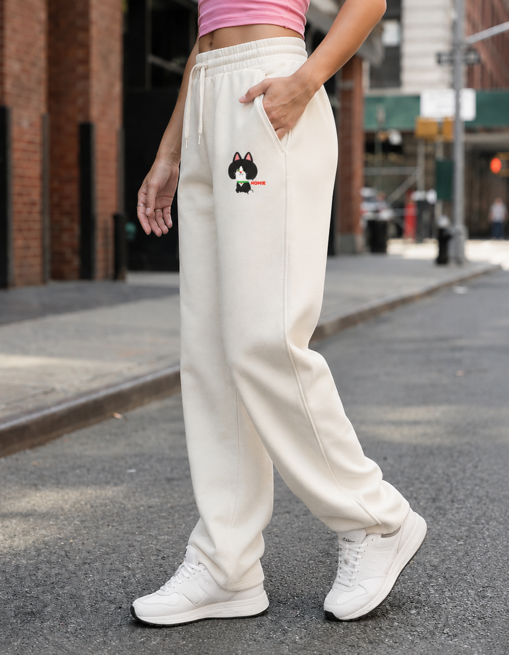 Person wearing white sweatpants with a small design on the side, standing on a city street.