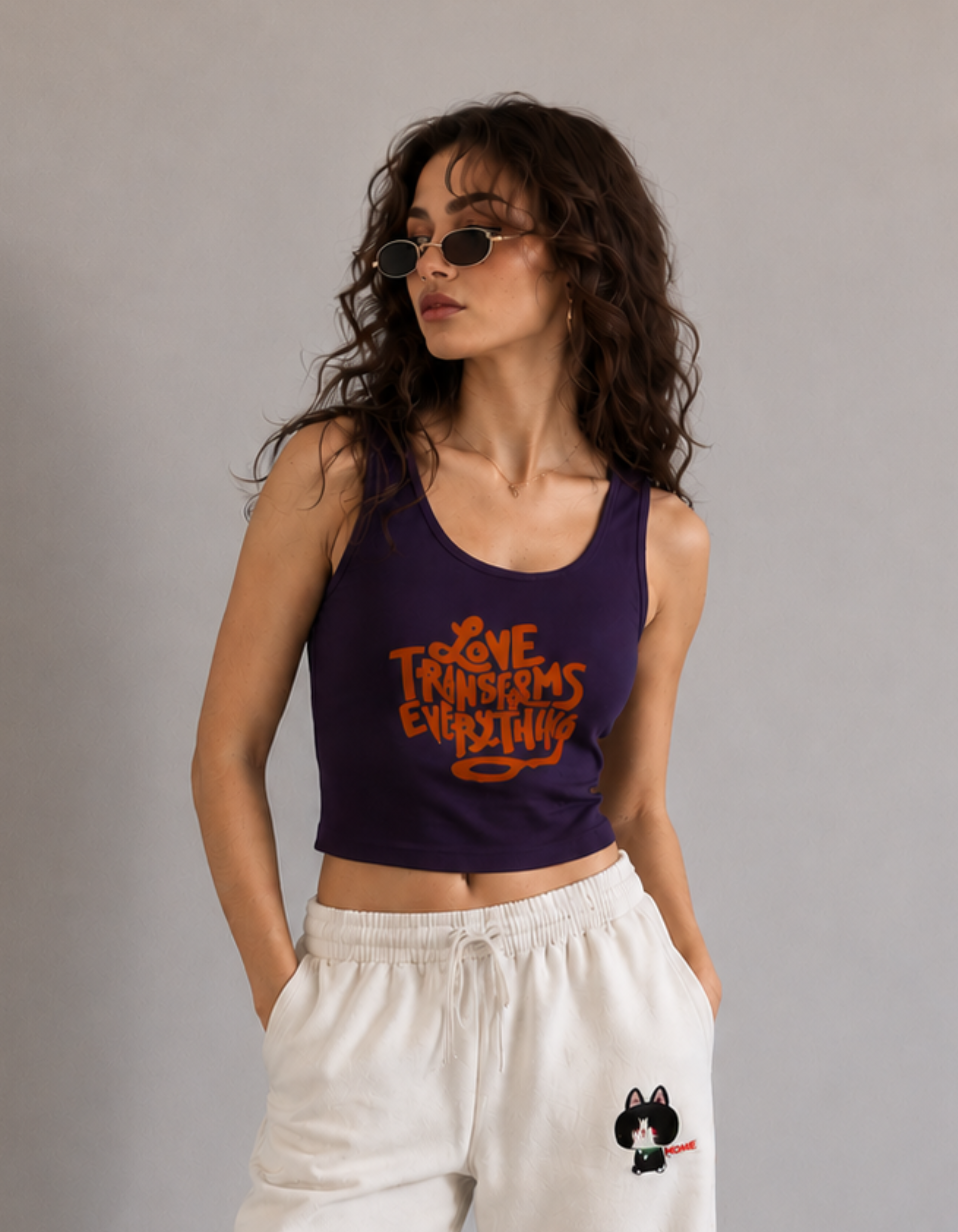 Woman wearing a purple tank top with orange text and white pants against a gray background