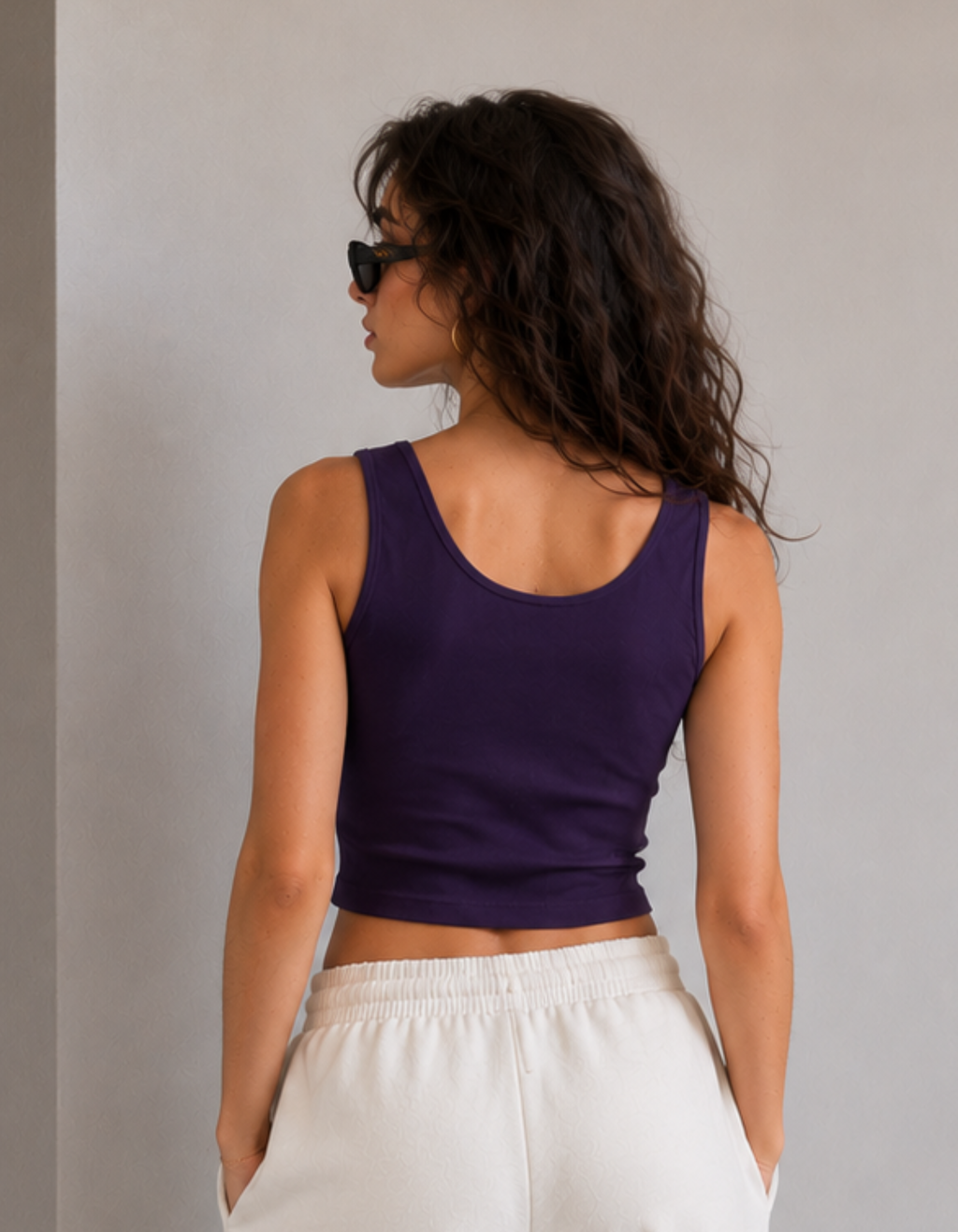 Woman wearing a purple tank top and white pants against a plain background