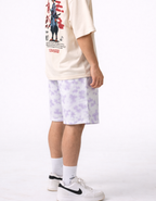 Person wearing a graphic t-shirt, light purple tie-dye shorts, and white sneakers on a white background