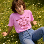 Person wearing a pink t-shirt with a graphic design sitting on grass with flowers.