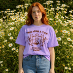 Person wearing a purple t-shirt with a graphic design in a field of flowers