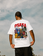 Person wearing a white t-shirt with Osaka-themed graphics against a cloudy sky.