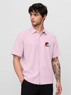 Man wearing a light pink short-sleeve shirt with a small graphic on a plain background