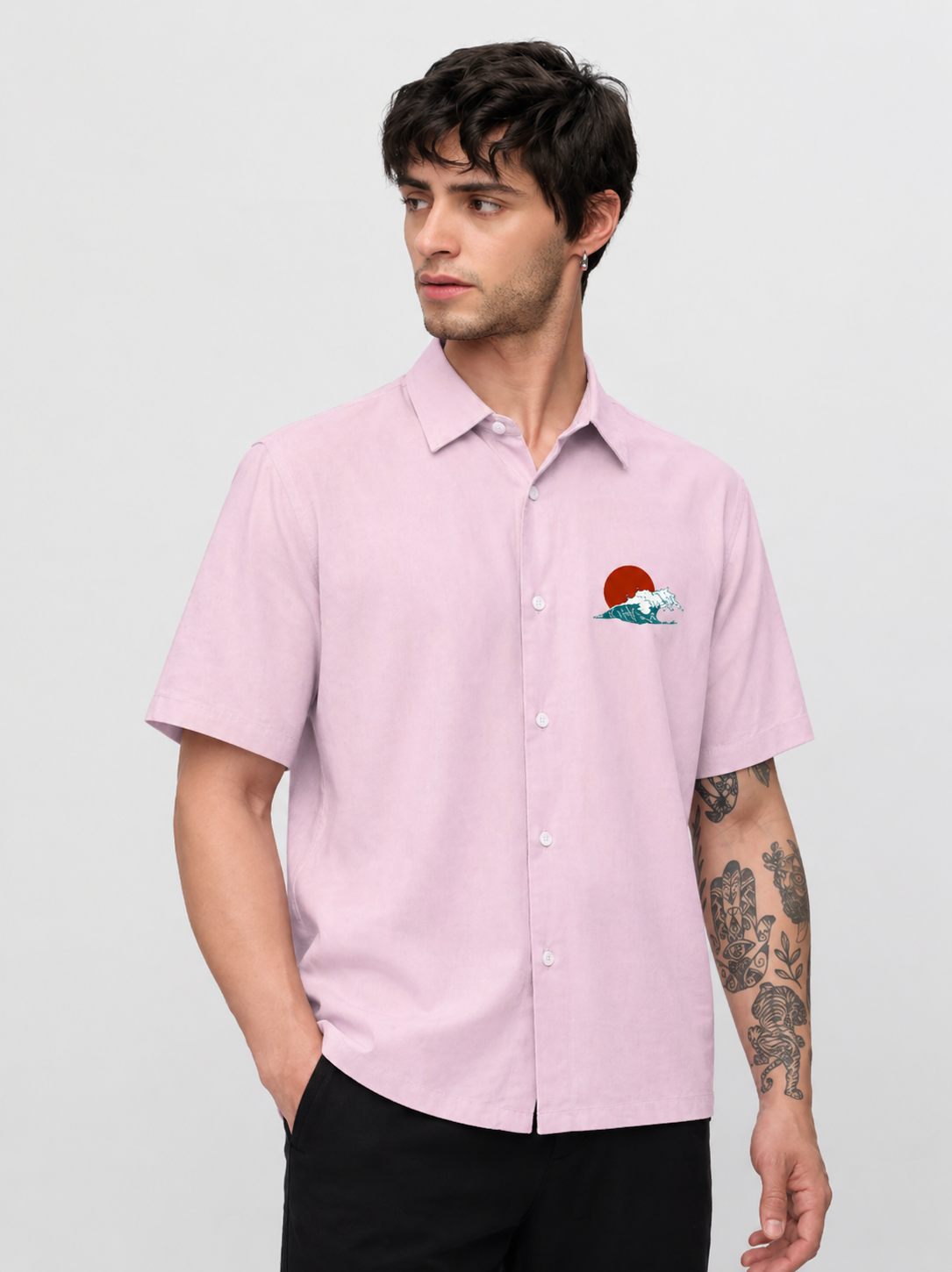 Man wearing a light pink short-sleeve shirt with a small graphic on a plain background