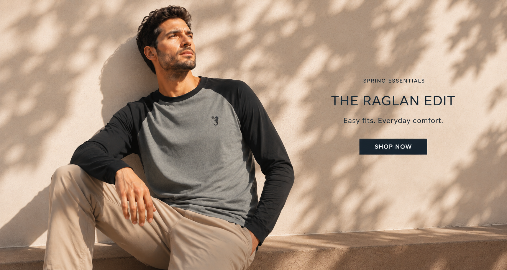 Man wearing a gray and black long-sleeve shirt sitting against a beige wall with 'The Raglan Edit' text.