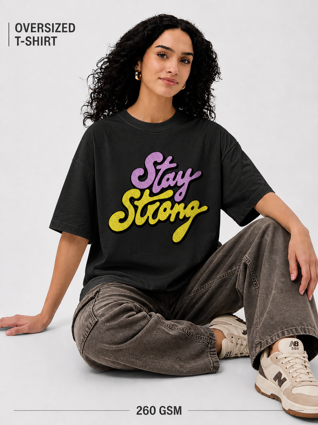 Person wearing an oversized t-shirt with 'Stay Strong' text, sitting on a light gray background.