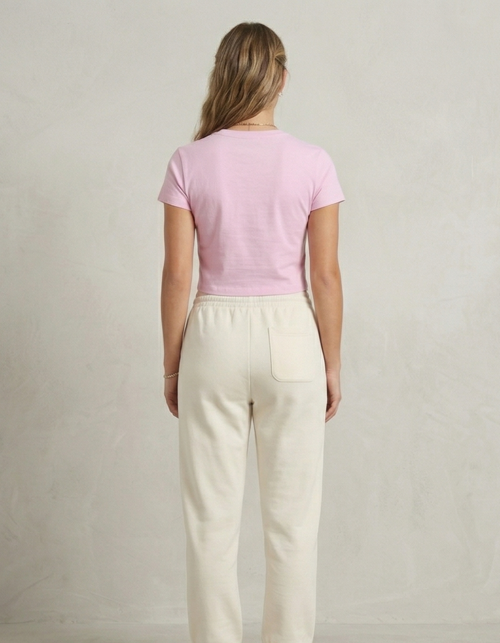 Woman wearing a pink top and beige pants against a plain background