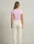 Woman wearing a pink top and beige pants against a plain background