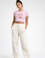 Woman wearing a pink graphic t-shirt and white pants on a white background