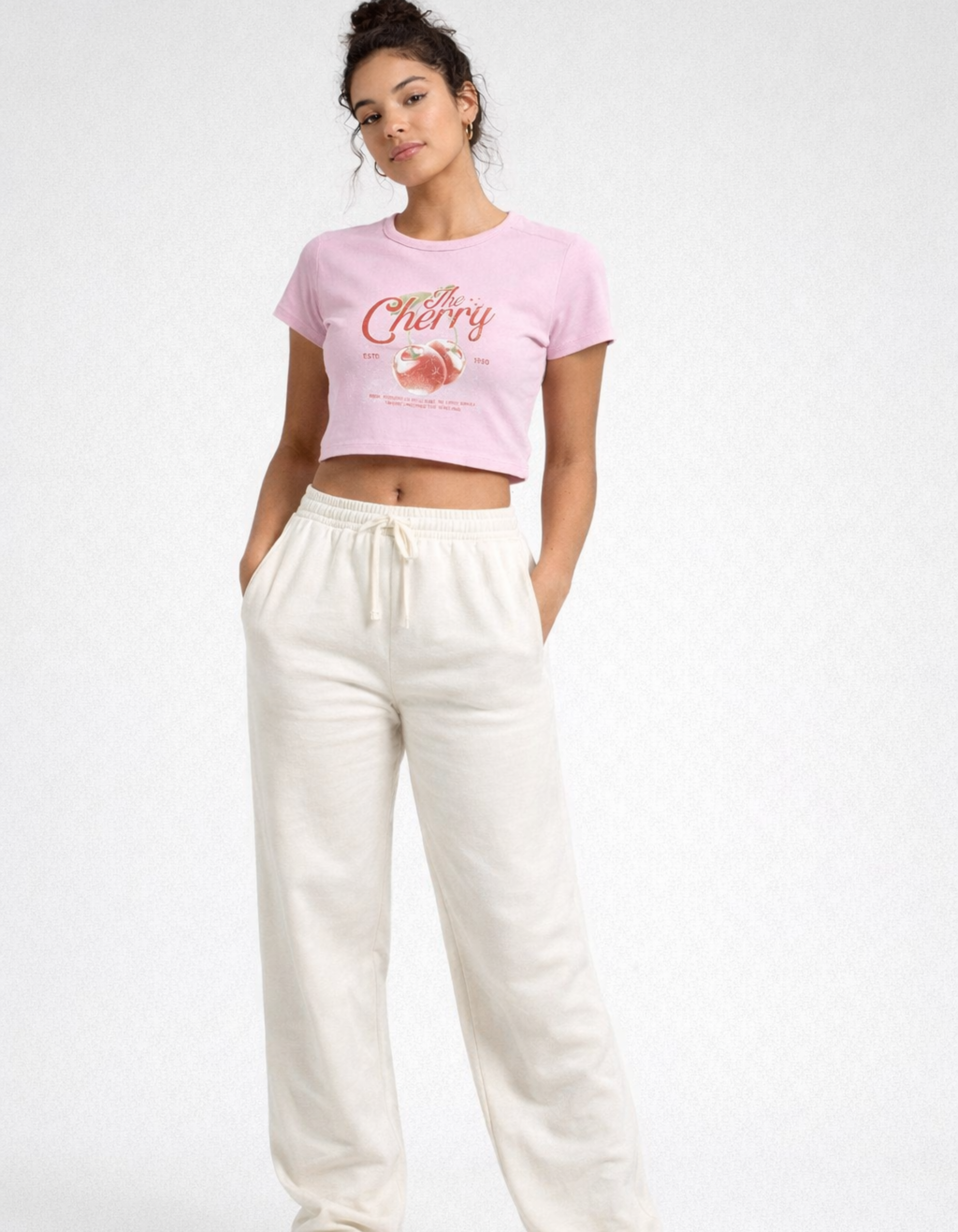 Woman wearing a pink graphic t-shirt and white pants on a white background
