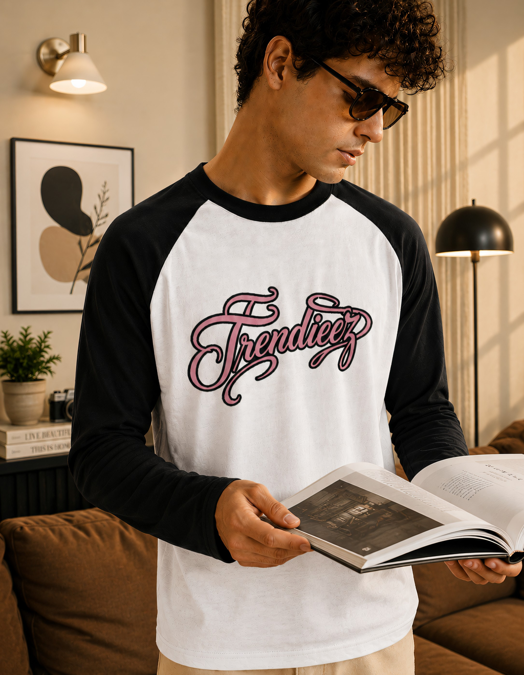 Man wearing a black and white 'Trendieez' shirt, holding an open book in a cozy living room.