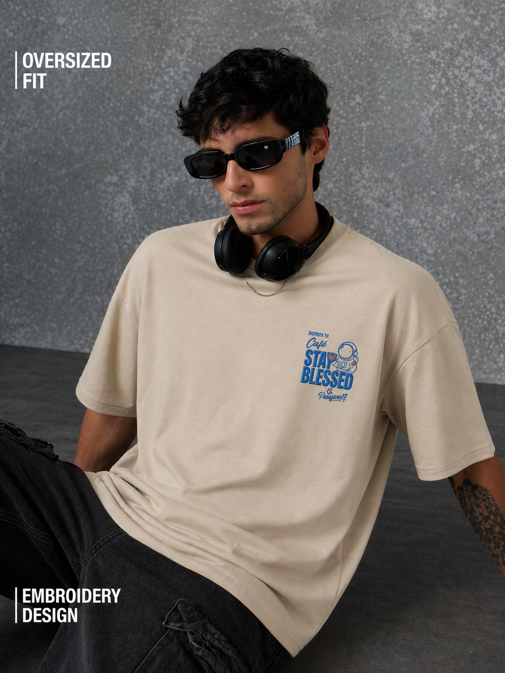 Man wearing a beige t-shirt with embroidery design, sitting against a gray background.