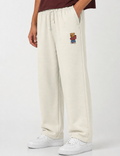 Person wearing cream sweatpants with a teddy bear patch on a white background