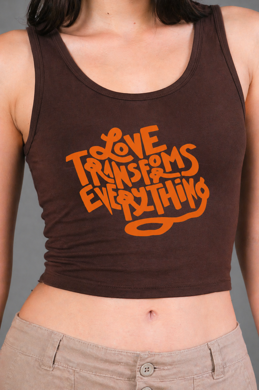 Brown tank top with orange text 'LOVE TRANSFORMS EVERYTHING' worn by a person.
